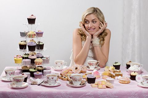Frau an einem Tisch, umgeben von Cupcakes und anderen Desserts