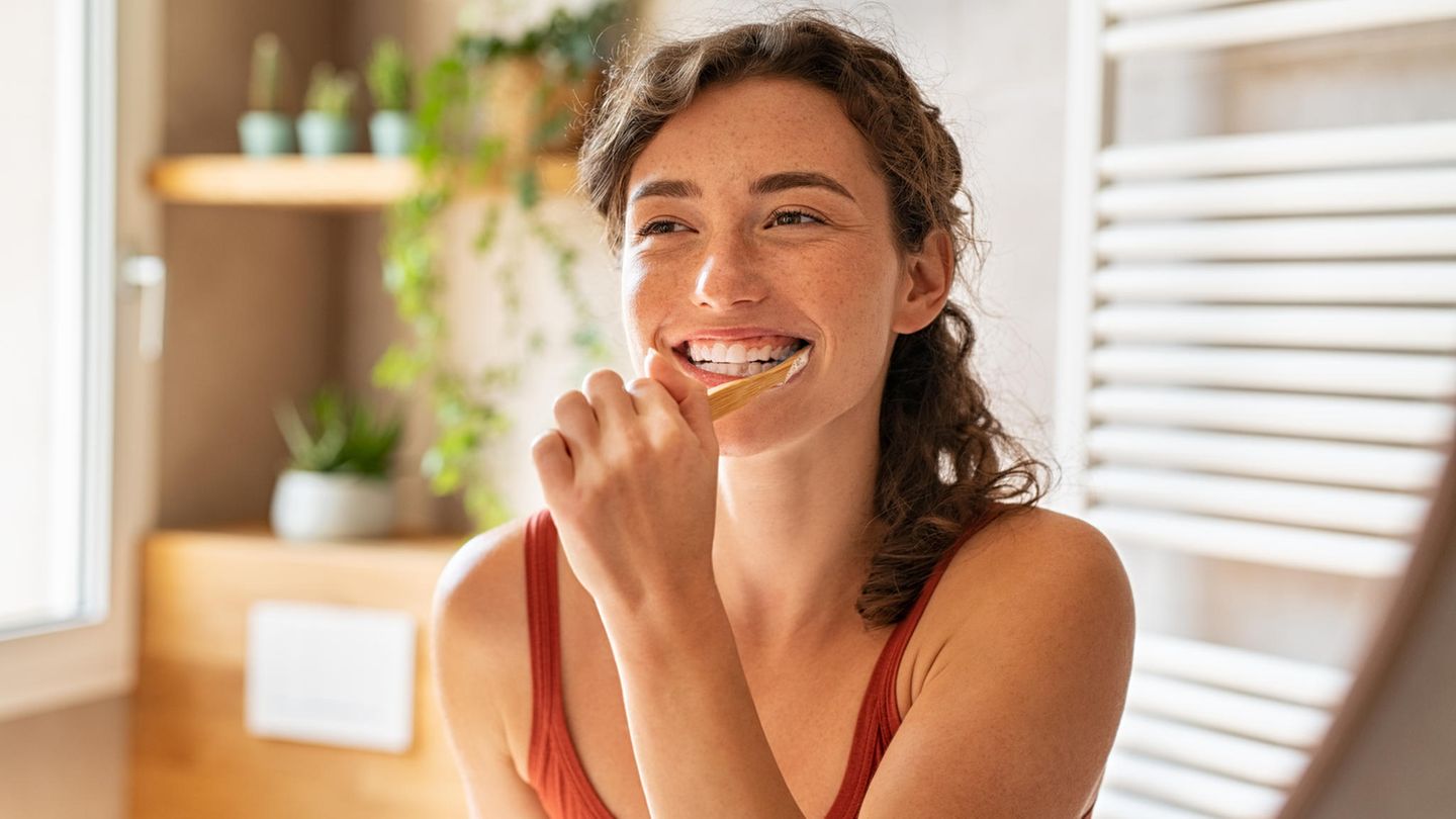 eine Frau putzt sich mit einer Holzzahnbürste die Zähne