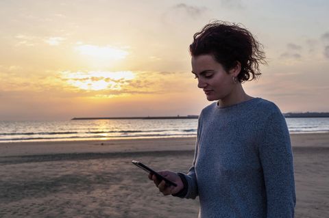 Frau schaut auf ihr Handy am Strand