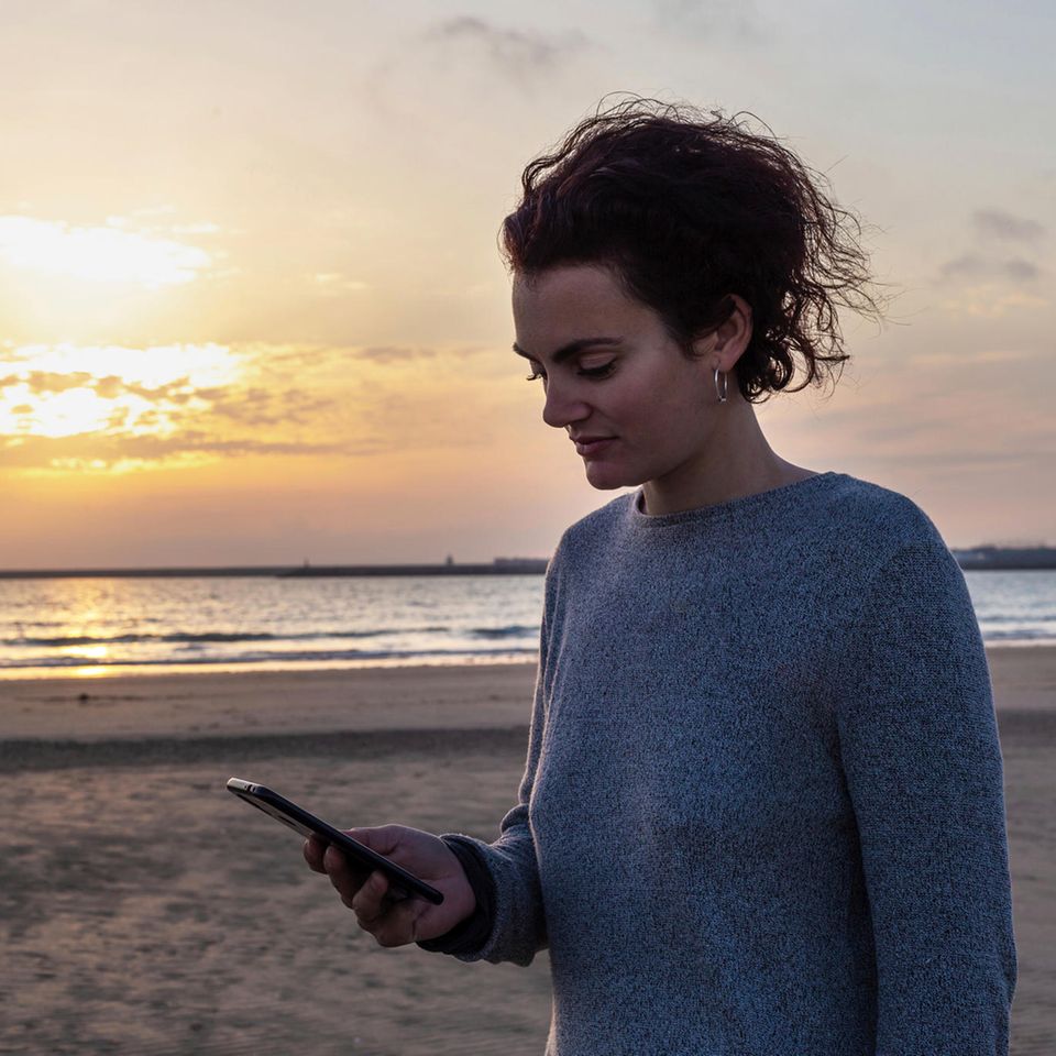 Frau schaut auf ihr Handy am Strand Frau schaut auf ihr Handy am Strand