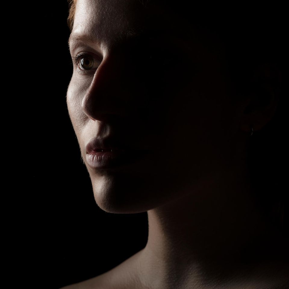 Portrait einer Frau vor schwarzem Hintergrund mit starkem Schatten auf einer Gesichtshälfte