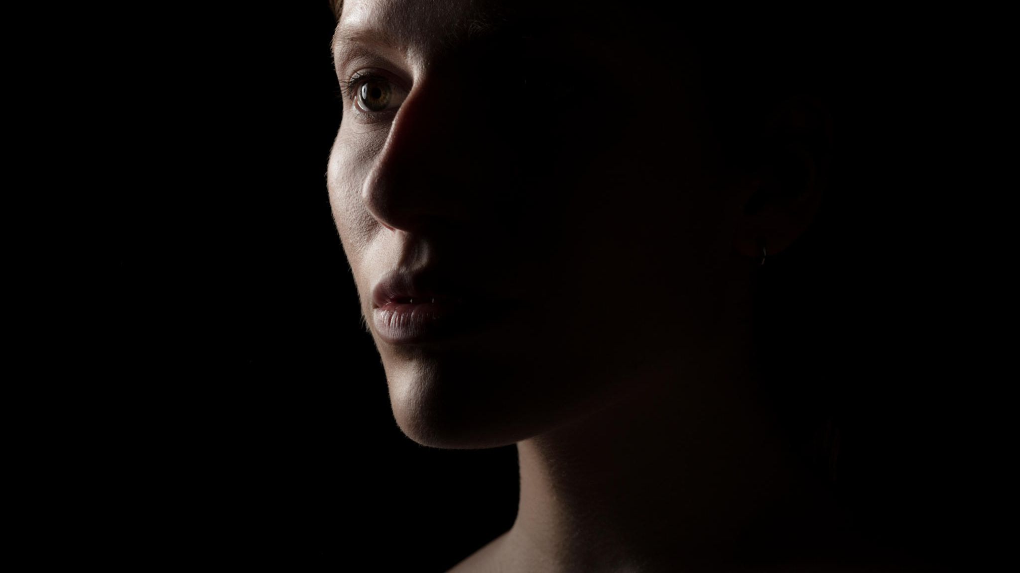Portrait einer Frau vor schwarzem Hintergrund mit starkem Schatten auf einer Gesichtshälfte
