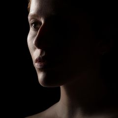Portrait einer Frau vor schwarzem Hintergrund mit starkem Schatten auf einer Gesichtshälfte