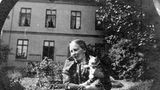 Eine Frau steht in einem Garten und trägt eine Katze auf dem Arm