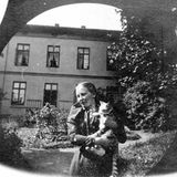 Eine Frau steht in einem Garten und trägt eine Katze auf dem Arm