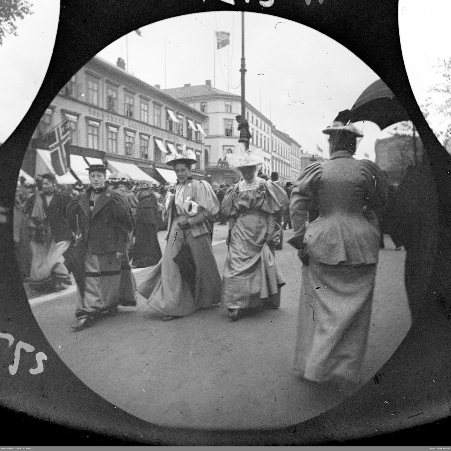 Blick auf eine belebte Straße, auf der im Vordergrund mehrere Frauen in Kleidern vorbeigehen