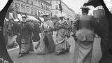 Blick auf eine belebte Straße, auf der im Vordergrund mehrere Frauen in Kleidern vorbeigehen