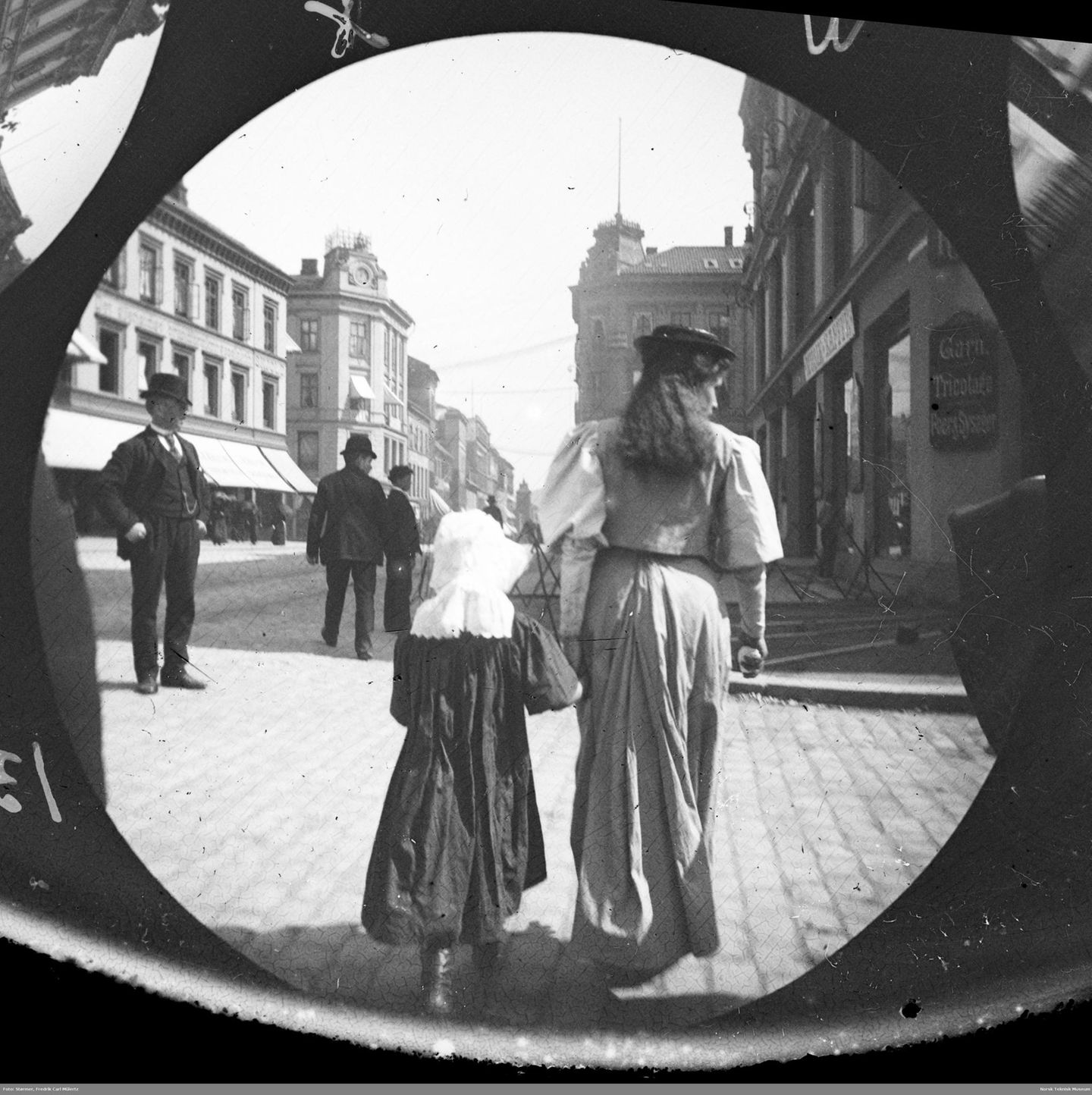 Auf dem Weg durch die Epochen Blick in eine Straßenflucht, im Vordergrund überquert, von hinten zu sehen, eine Frau mit einem Kind die Fahrbahn