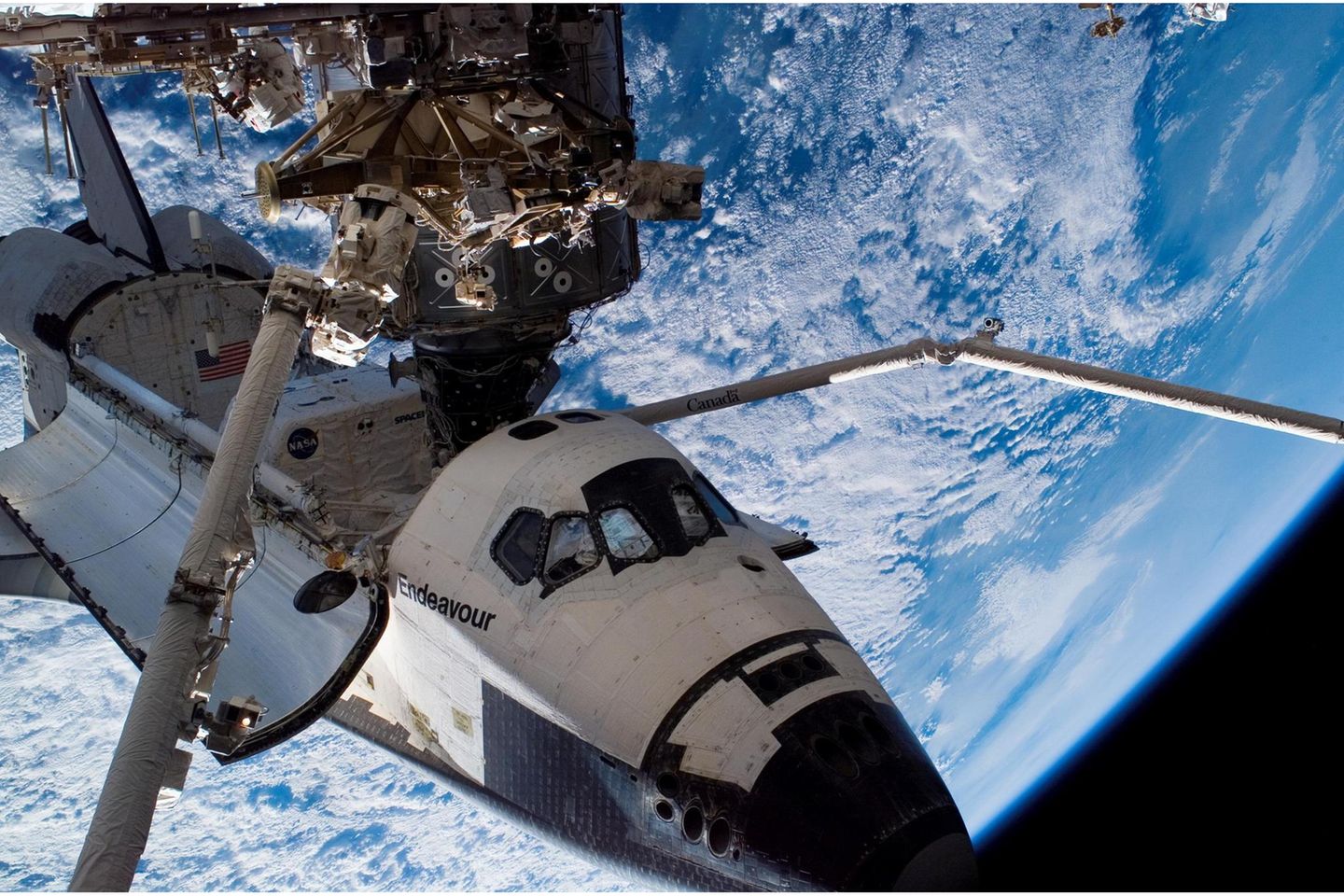 Über 420 Tonnen schwer, 109 Meter lang, fast so geräumig wie ein Jumbojet und gespickt mit 350 000 Sensoren: Die mit Abstand größte Struktur, die die Menschheit bislang im Erdorbit montiert hat, die Internationale Raumstation ISS, ist ein Koloss und ein fragiles Objekt zugleich. Nur wenige Millimeter Aluminium und ein paar schützende Kunststoffschichten trennen die Bewohner*innen vom Vakuum des Weltalls.  Bislang klappt das gut: Seit November 2000 ist die Raumstation, für deren Aufbau und Betrieb sich fünfzehn Staaten zusammengeschlossen haben, permanent bewohnt. Insgesamt 42 Raumflüge, davon allein 37 mit den US-amerikanischen Spaceshuttles, waren nötig, um die Wohnmodule, Solarzellen und weiteren Komponenten in eine Höhe von gut 400 Kilometern zu bringen. Es sollte nicht bei diesen Missionen bleiben: Die Station, auf der im Normalfall sieben Menschen wohnen, forschen und arbeiten, ist wartungsintensiv. Mal fällt eine der Toiletten aus, mal muss ein Raumanzug erneuert werden, mal spielt die Stromversorgung verrückt. Trotzdem soll die ISS bis ins Jahr 2030 den Betrieb durchhalten. Erst dann könnten kleinere, kommerzielle Stationen die Aufgaben des fragilen Kolosses übernehmen.  Im Bild: Die Raumfähre "Endeavour" dockt im August 2007 an die Internationale Raumstation an. Sie liefert einen Teil der tragenden Gitterstruktur. Es ist der 26. Flug zum Aufbau des orbitalen Außenpostens