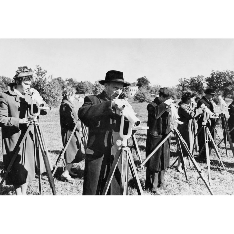 Die Sowjets erleben Anfang der 1960er-Jahre eine gewaltige Weltraum-Euphorie: Gerade einmal zwei Jahre ist es her, dass die UdSSR den ersten Satelliten in eine Umlaufbahn gebracht hat. 92 Tage lang kreiste Sputnik 1 um die Erde, beobachtet von sowjetischen Wissenschaftler*innen und bestaunt von der ganzen Welt. Die ersten Lebewesen, darunter die Hunde Strelka und Belka, kehren im selben Jahr unbeschadet von einem Ausflug in den Orbit zurück. Und auch der Start von Juri Gagarin, des ersten Menschen im All, in die Erdumlaufbahn ist nur noch ein Jahr entfernt.  Es ist die goldene Ära der sowjetischen Raumfahrt – und das zu einer Zeit, als die Raketen der Vereinigten Staaten reihenweise auf der Startrampe explodieren. Verantwortlich für den sowjetischen Erfolg ist Chefkonstrukteur Sergej Koroljow. Bilder des genialen Raketenbauers gibt es zu dieser Zeit allerdings kaum – schon gar nicht auf Neujahrskarten: Die UdSSR hält Koroljows Existenz geheim, aus Angst vor Attentaten westlicher Geheimdienste.  Im Bild: Sowjetische Forschende verfolgen 1957 Sputnik 1