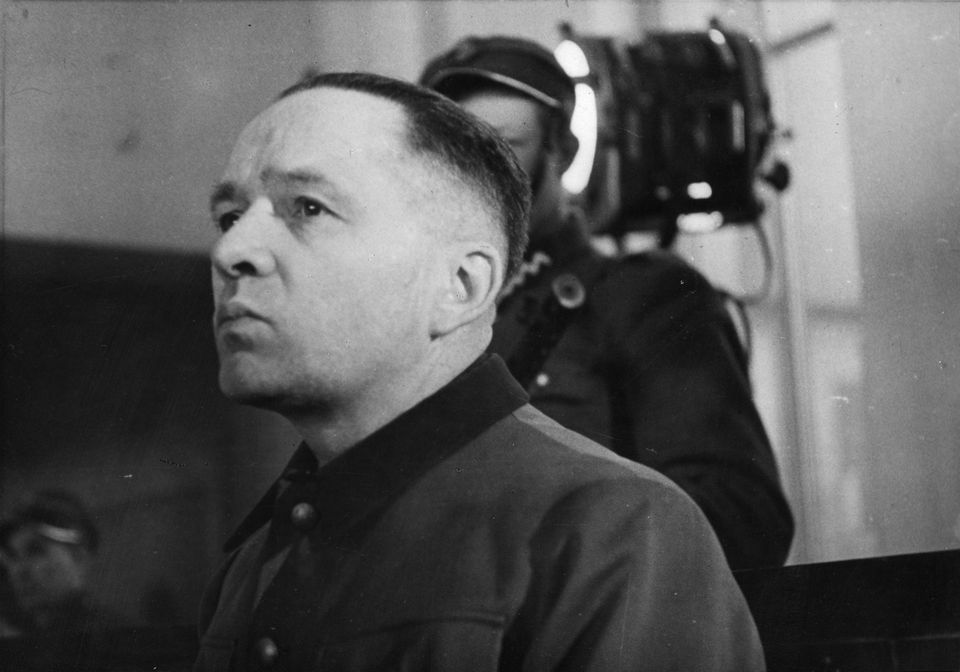 Porträt von Rudolf Höß während seines Prozesses, im Hintergrund ist ein Uniformierter zu sehen Porträt von Rudolf Höß während seines Prozesses, im Hintergrund ist ein Uniformierter zu sehen