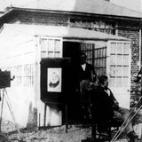 Mehrere Männer mit Geräten vor einem Gebäude, dazwischen ist eine Art Gemälde aufgestellt