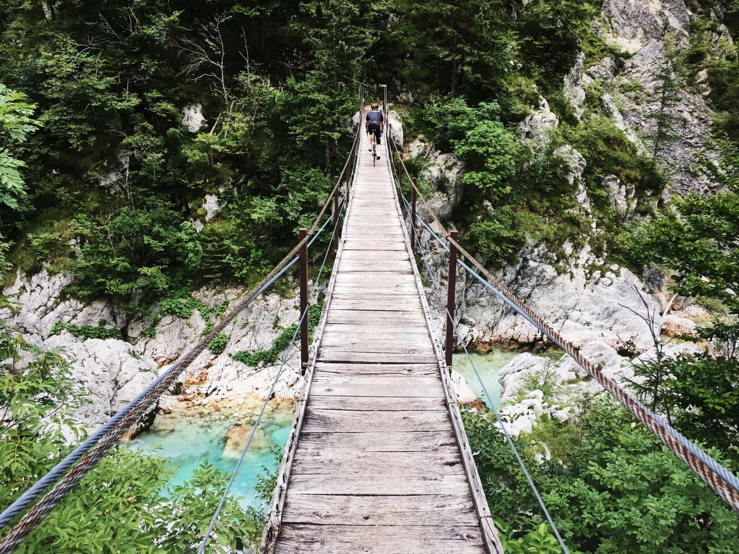 Hängebrücke über Fluss und Felsen mit Fahrradfahrer