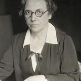 sw-Foto einer Frau mit Brille und hochgesteckten Haaren  in einem Kostüm mit weisser Bluse