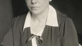 sw-Foto einer Frau mit Brille und hochgesteckten Haaren  in einem Kostüm mit weisser Bluse