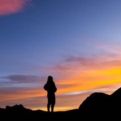 Rückenansicht eines Mannes der auf einem Berg steht und in die Ferne guckt