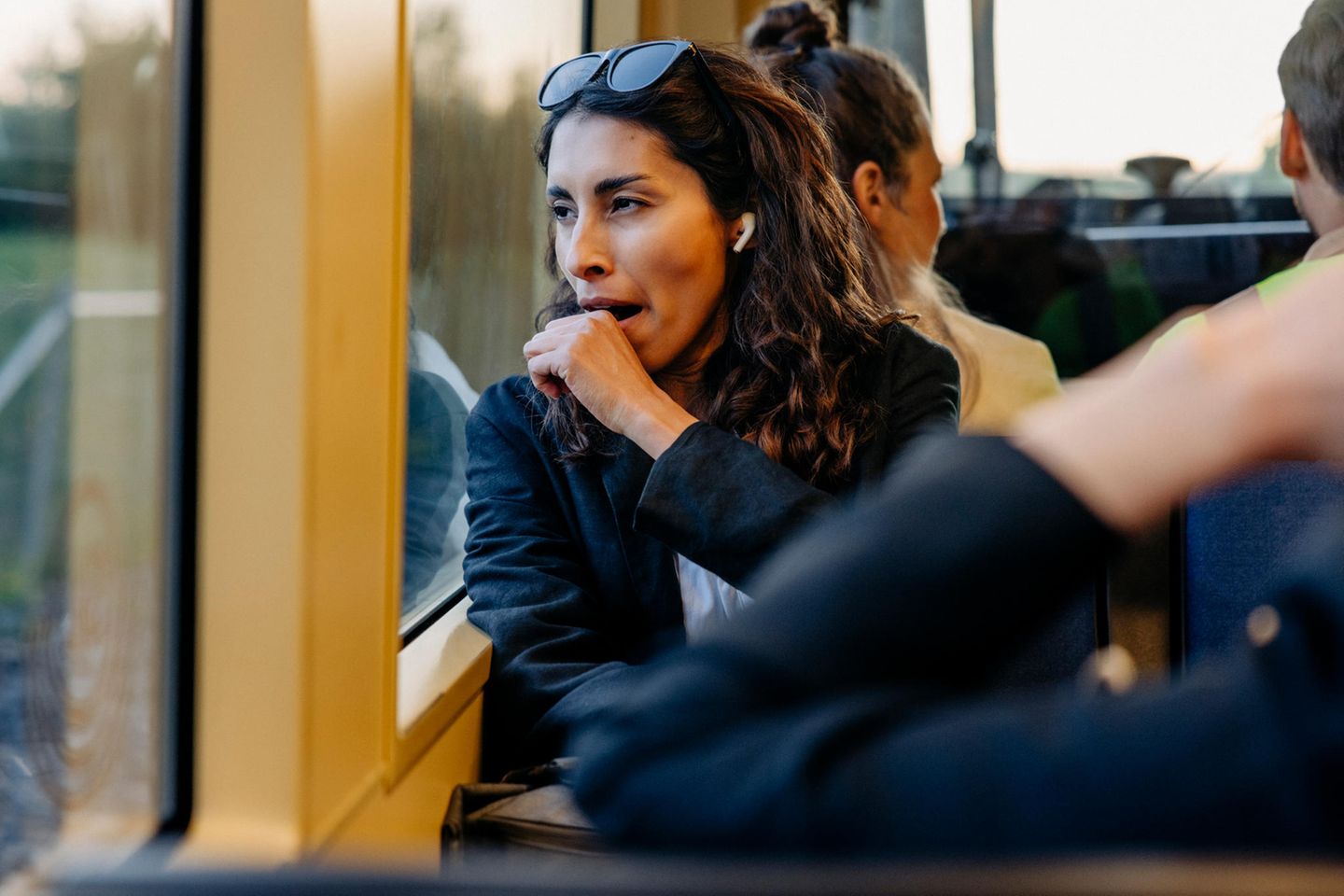 Frau mit dunklen Locken sitzt gähnend in der Bahn