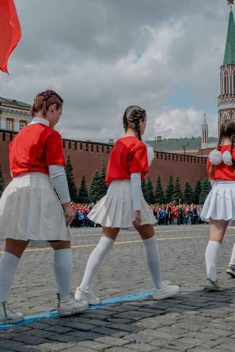 Jugendliche mit roten Pullovern und weißen Röcken gehen über den Roten Platz in Moskau