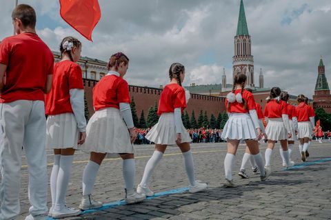 Jugendliche mit roten Pullovern und weißen Röcken gehen über den Roten Platz in Moskau