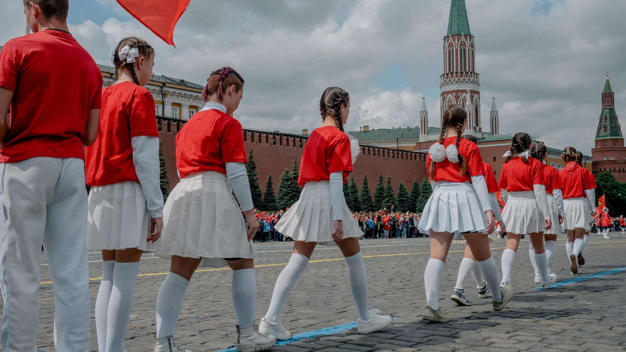Jugendliche mit roten Pullovern und weißen Röcken gehen über den Roten Platz in Moskau