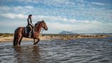 Reitende Frau im seichten Meerwasser am Strand