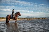 Reitende Frau im seichten Meerwasser am Strand