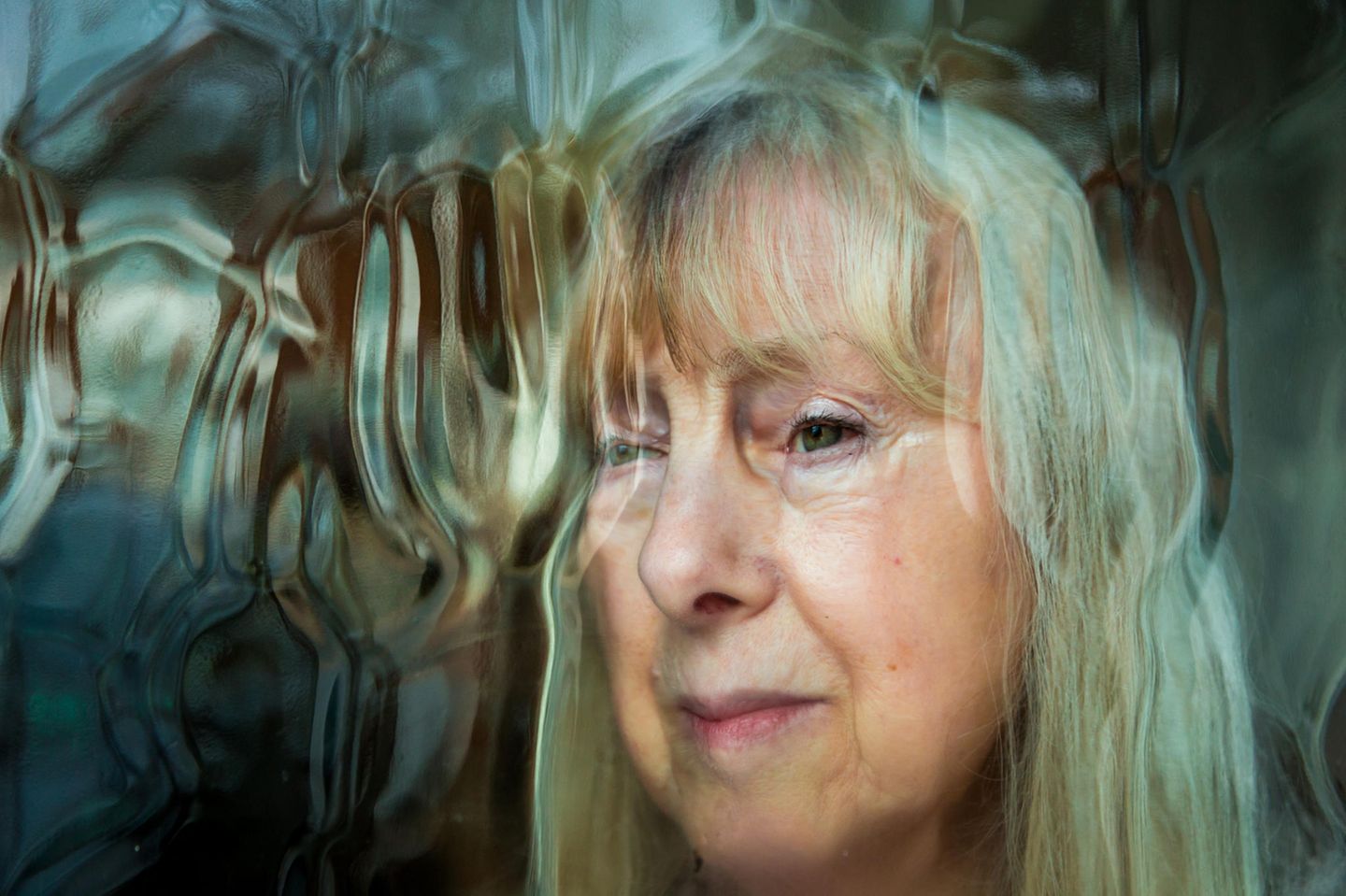 Leicht verzerrtes Gesicht einer Senioren mit Delir hinter einer Glasscheibe.  Leicht verzerrtes Gesicht einer Senioren mit Delir hinter einer Glasscheibe.