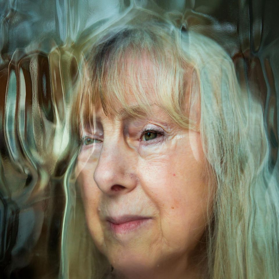 Leicht verzerrtes Gesicht einer Senioren mit Delir hinter einer Glasscheibe.