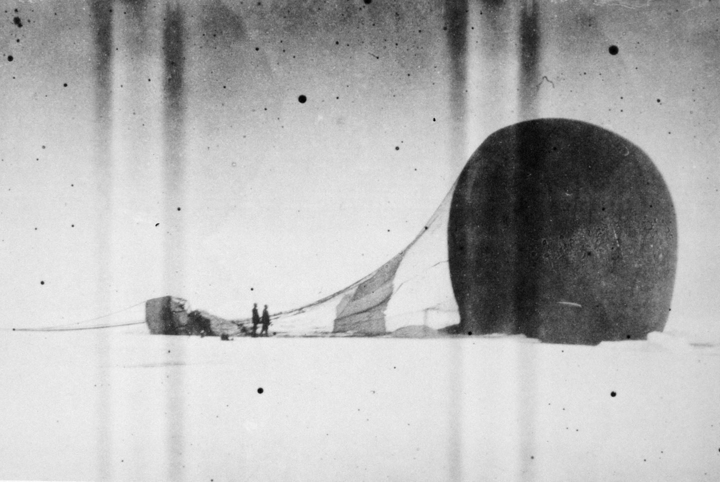 Ein Ballon liegt seitlich abgesunken auf dem Eis, die Gondel und zwei Personen befinden sich links davon