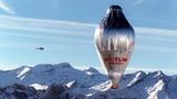 Ein silbern glänzender, länglicher Ballon mit einer roten Gondel überquerte schneebedeckte Alpengipfel