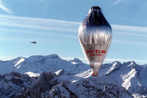 Ein silbern glänzender, länglicher Ballon mit einer roten Gondel überquerte schneebedeckte Alpengipfel