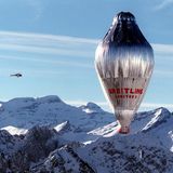 Ein silbern glänzender, länglicher Ballon mit einer roten Gondel überquerte schneebedeckte Alpengipfel