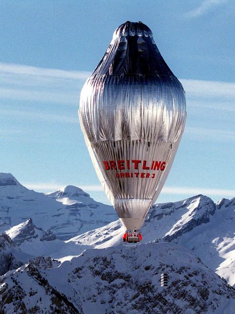 Ein silbern glänzender, länglicher Ballon mit einer roten Gondel überquerte schneebedeckte Alpengipfel
