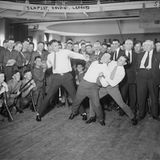 Umringt von Zuschauern, gekleidet in Hemd und Krwatte schlagen Houdini und zwei Profiboxer zum Schein aufeinander ein