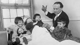 Houdini steht im Anzug an einem eisernen Krankenhausbett mit fünf Kindern und unterhält sie mit einem Kaninchen