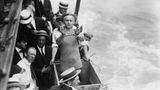 Umringt von Zuschauern steht Houdini in einer Holzkiste über dem East River und präsentiert seine Fesseln
