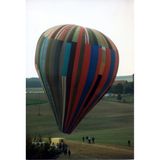 Ein aus bunten Streifen zusammengesetzter Heißluftballon schwebt kurz über einer Wiese