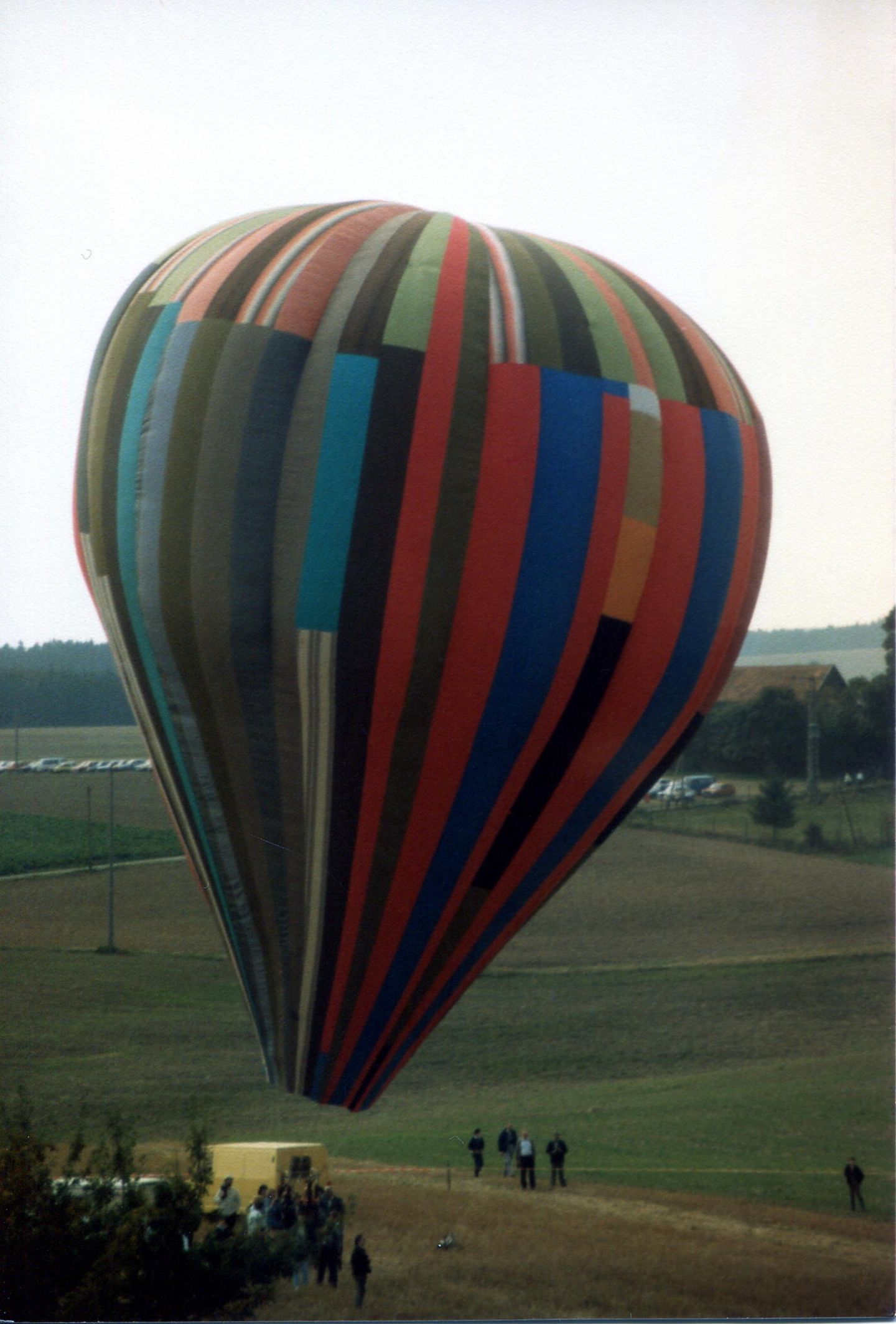 Ein aus bunten Streifen zusammengesetzter Heißluftballon schwebt kurz über einer Wiese