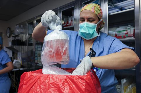 Krankenschwester hebt Gefäß mit roter Flüssigkeit aus einer Box