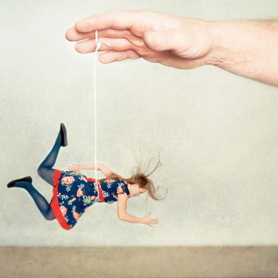 Frau hängt an einer Schnur und wird von einer Hand hochgehalten