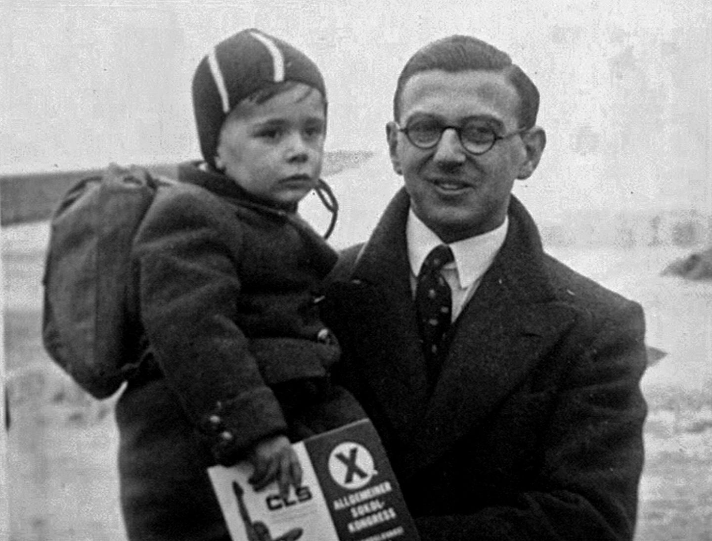 Nicholas Winton in Wintermantel und Krawatte hält lächelnd einen kleinen, ebenfalls warm angezogenen Jungen auf dem Arm  Nicholas Winton in Wintermantel und Krawatte hält lächelnd einen kleinen, ebenfalls warm angezogenen Jungen auf dem Arm