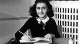 Anne Frank sitzt an einem Tisch, ein aufgeschlagenes Heft zum Schreiben vor sich