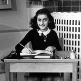 Anne Frank sitzt an einem Tisch, ein aufgeschlagenes Heft zum Schreiben vor sich