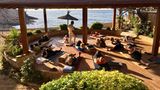 Menschen machen Yoga auf Yogamatten unter Sonnenschirmen auf Terrasse, dahinter das Meer