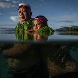 Großvater steht im brusthohen Wasser mit seinem Enkel im Arm