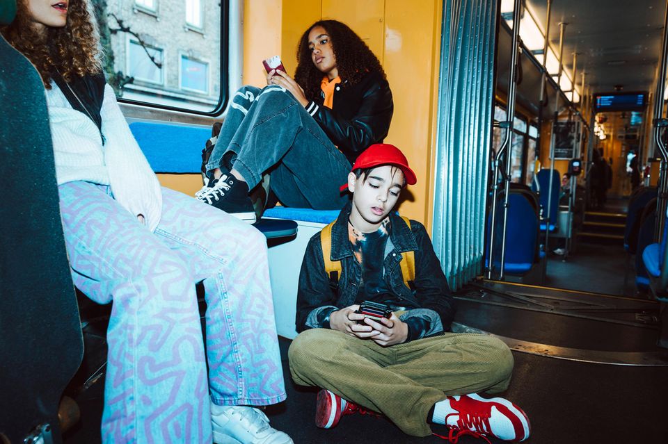 Drei Jugendliche spielen sitzend am Handy in der Bahn