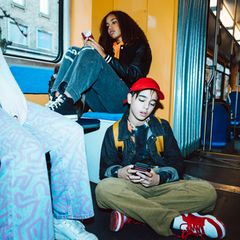 Drei Jugendliche spielen sitzend am Handy in der Bahn