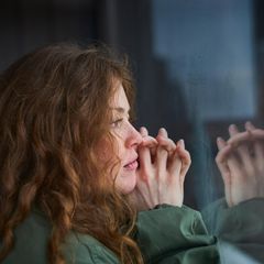 Frau schaut mit gefalteten Händen aus dem Fenster