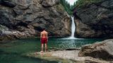 Mann in roter Badehose steht an den Buchenegger Wasserfällen