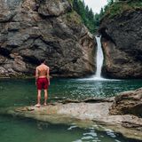 Mann in roter Badehose steht an den Buchenegger Wasserfällen